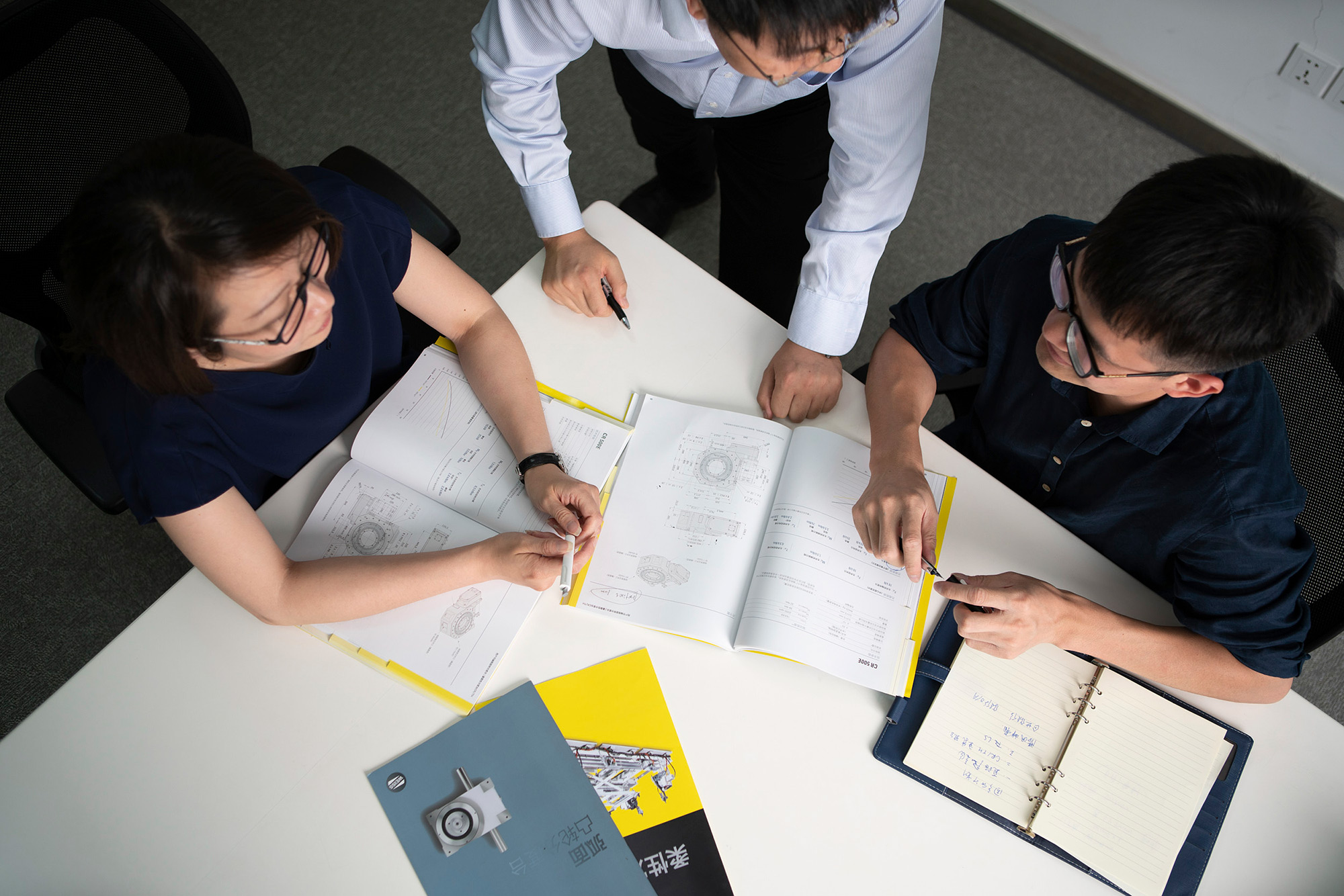 Corporate Photography Services. A team of engineers meets in an office to discuss blueprints and problem-solving as part of a corporate photography campaign.