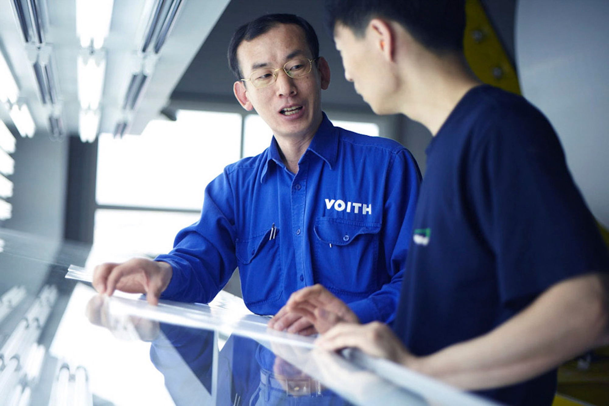 Engineers at work photography services Two Voith engineers engage in a conversation about paper production quality, captured for an industrial engineering photography campaign.