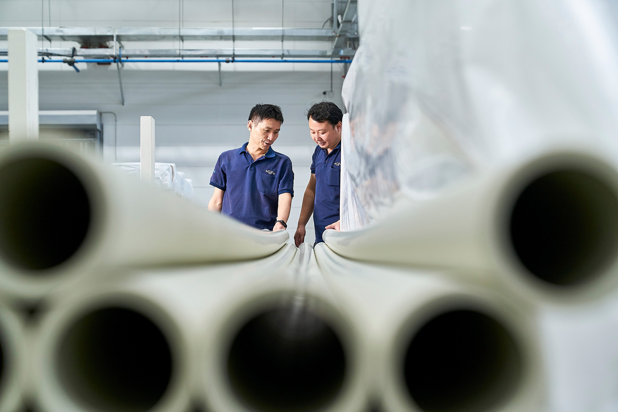 Engineers at work photography services Two engineers inspect PVC pipes on the factory floor, captured for an industrial engineering photography campaign.