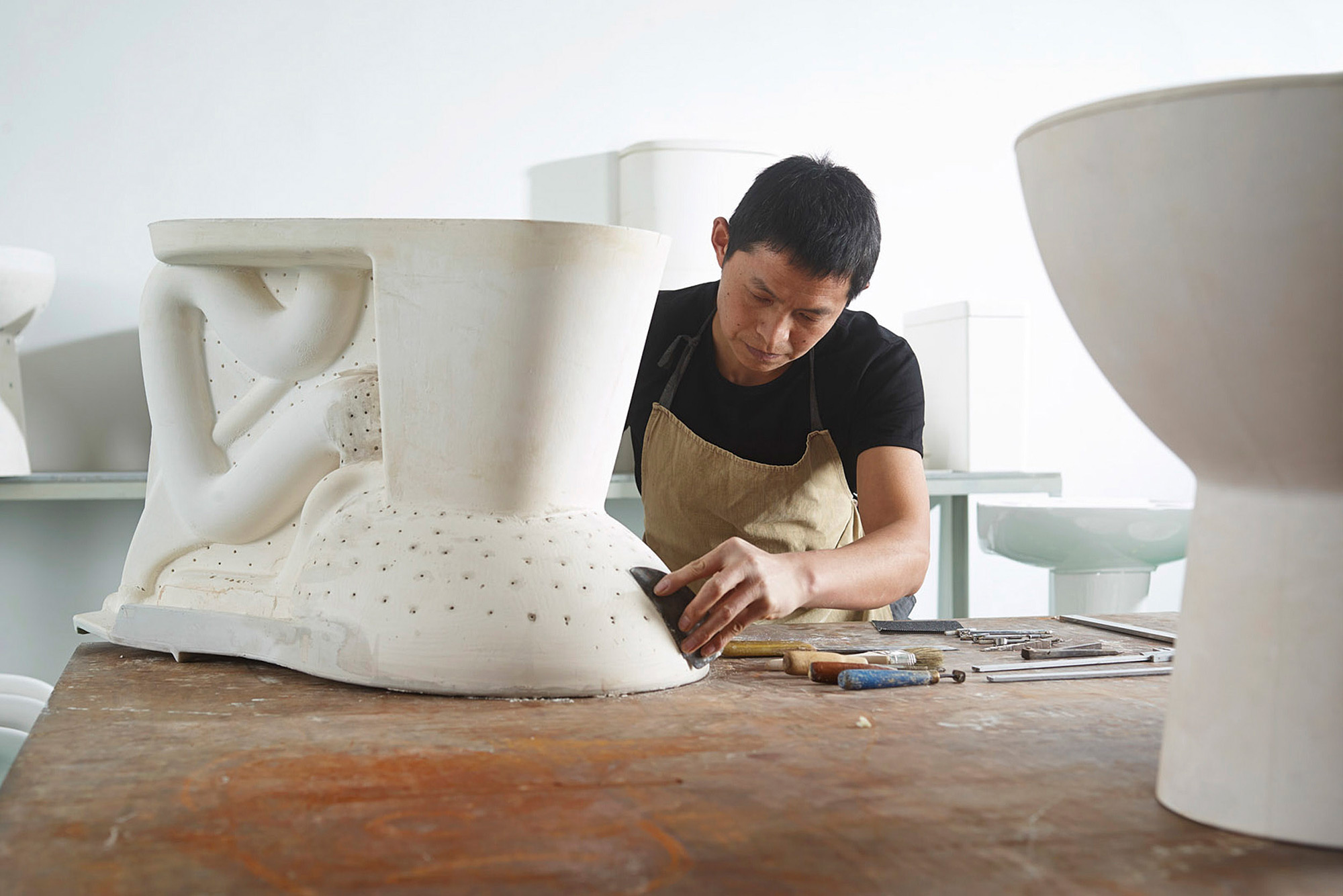 Artisan photography services Worker sculpting porcelain to craft a toilet, highlighted in an artisan photography campaign.