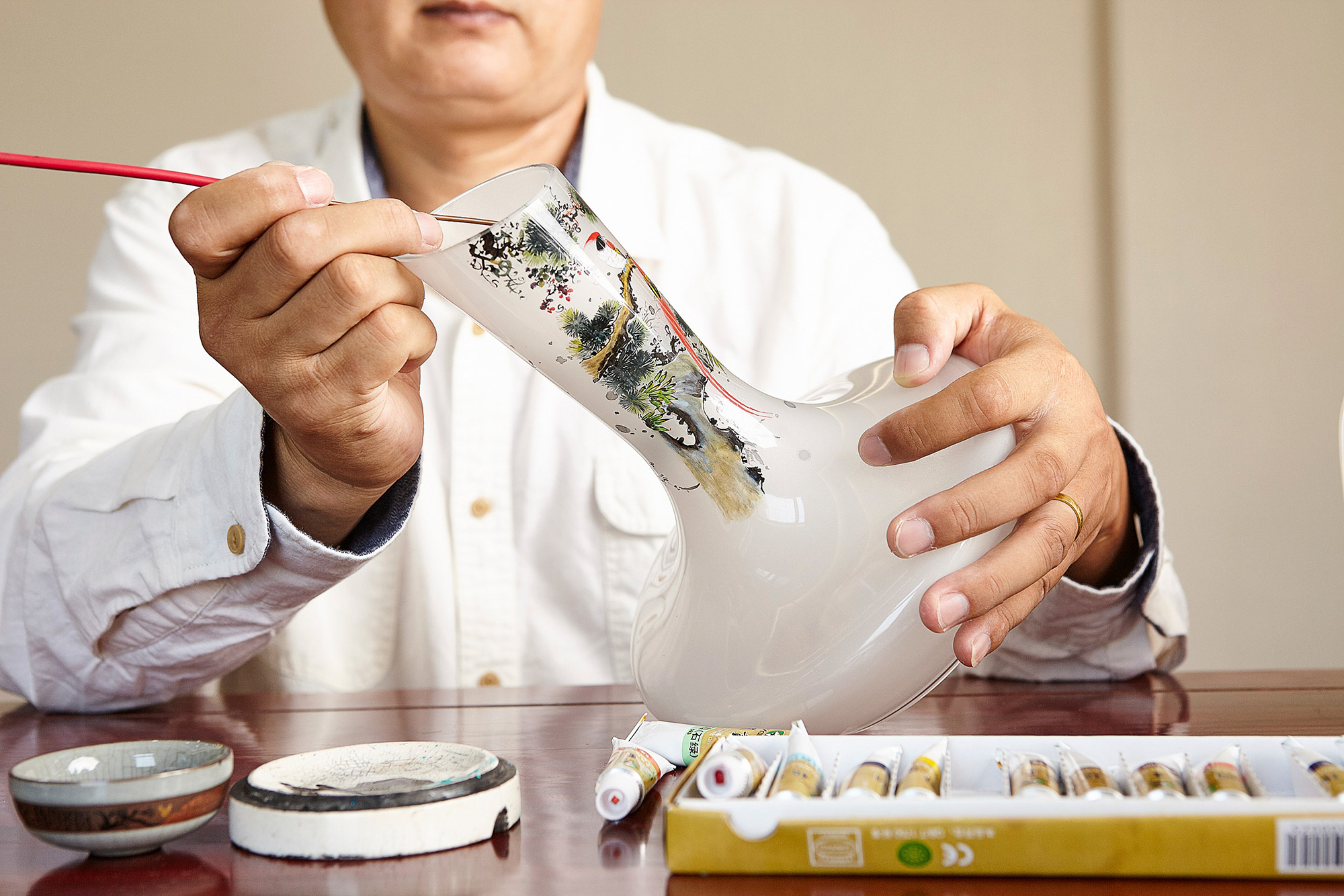 Artisan photography services Painter crafting traditional Chinese art on a glass vase, captured for an artisan photography campaign.