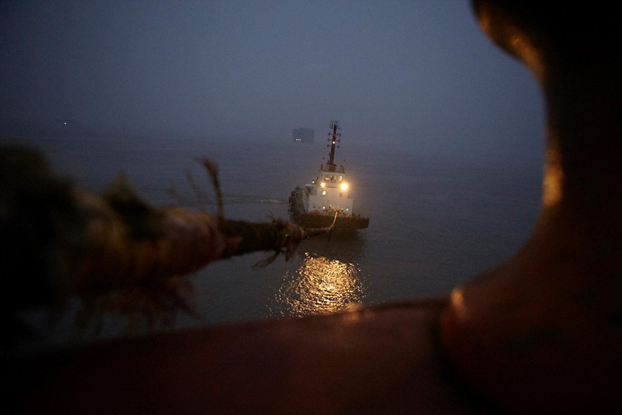 Dock engineer operates machinery as it offloads from Dockwise’s floating super palette. Industrial naval photography services Tugboat in operation during early morning, accompanied by a dock engineer offloading machinery from Dockwise's floating super palette, captured for an industrial naval photography campaign.