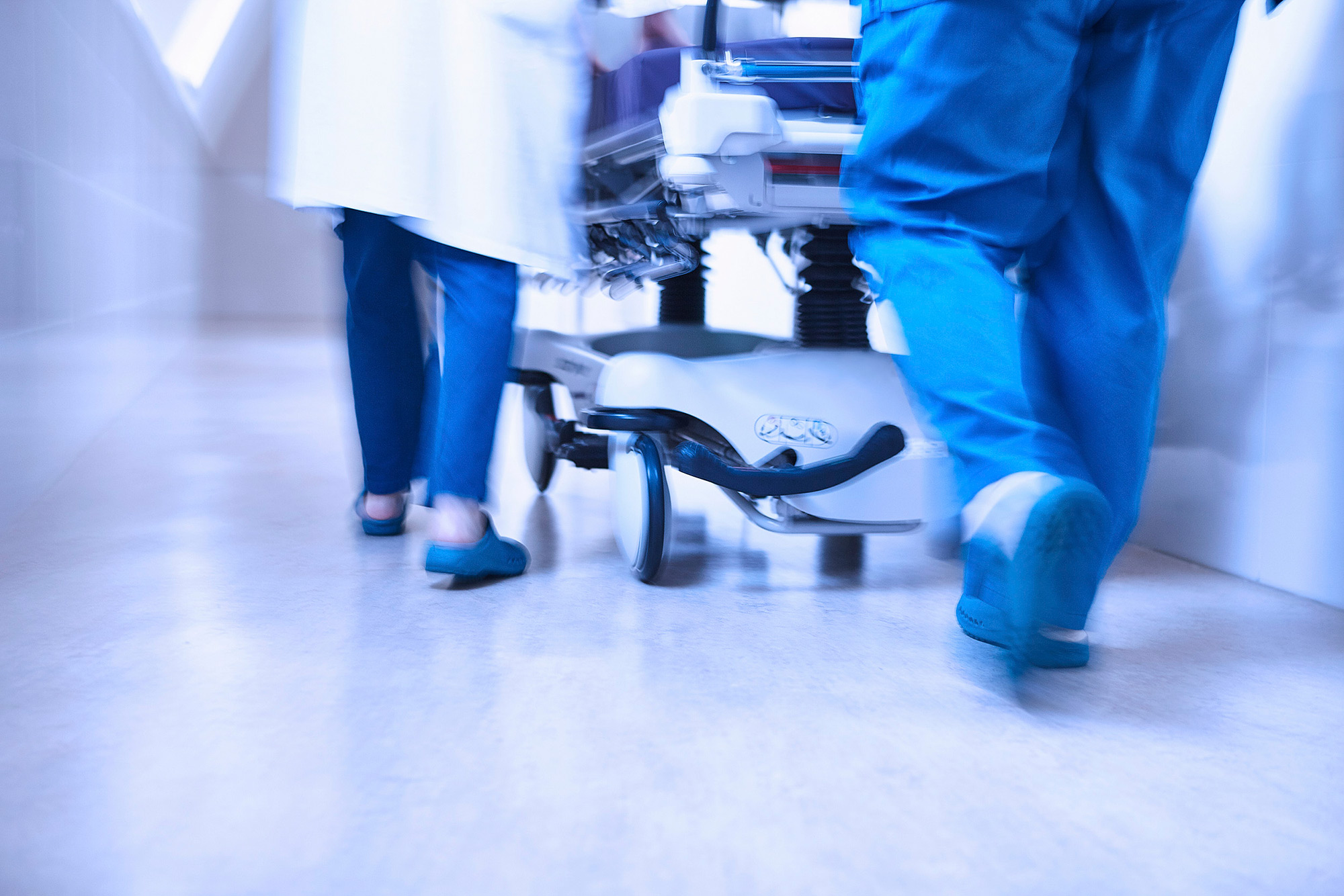 Medical Science Photography Services Blurry scene of a hospital bed being pushed down a hallway by medical staff, captured for Medical Science Photography Services.