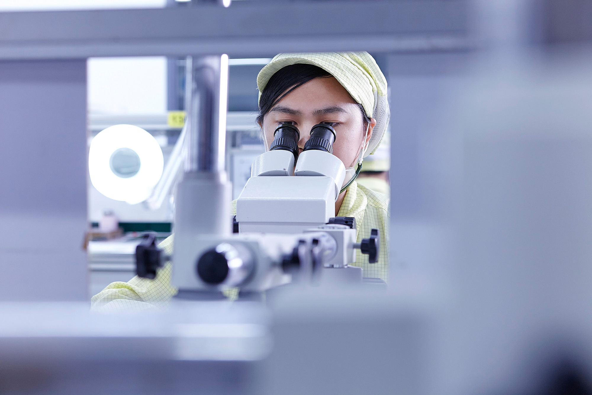 Science & Technology Photography services Dedicated female engineer examining through a microscope for quality assurance services at Flextronics, showcasing our science and technology photography services.