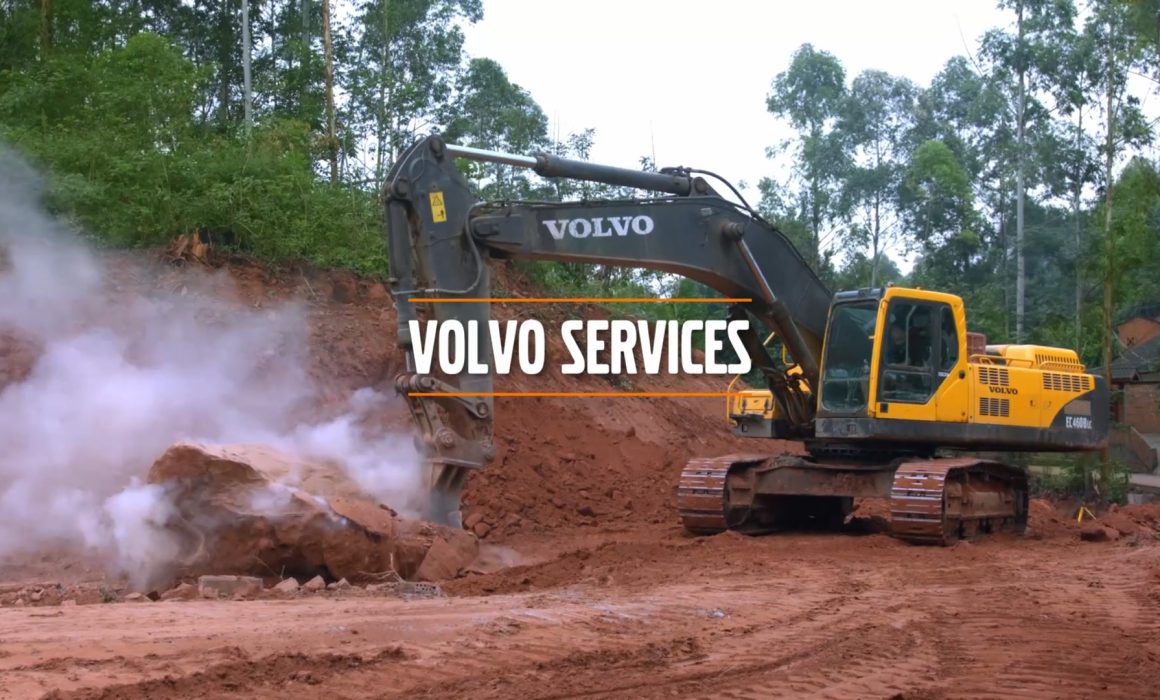 An excavator breaks a rock near a forrest with the "Volvo Services" slogan. This image is used as a cover image for the professional documentary video associated with it. We speak the Volvo Construction Equipment owners.