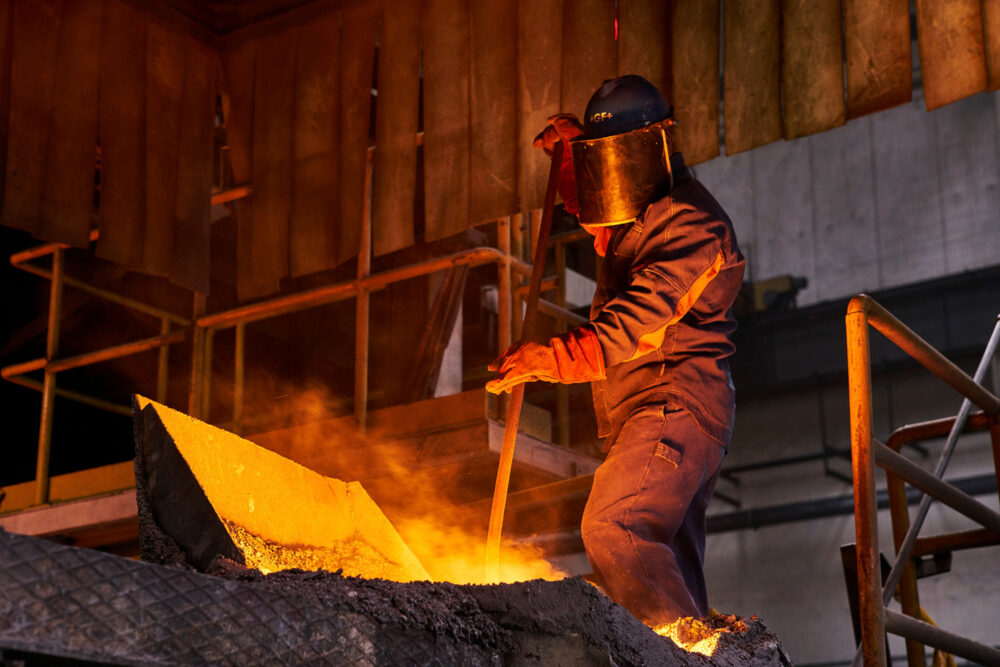 Worker stirring molten metal, featured in industrial photography for Georg Fischer.