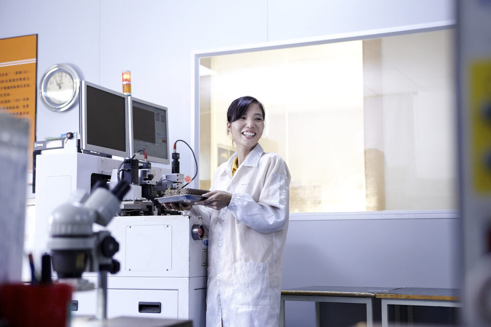 Clean room factory floor featuring a female engineer with a tray of LED lights in a science and technology image produced for an LED lighting factory.