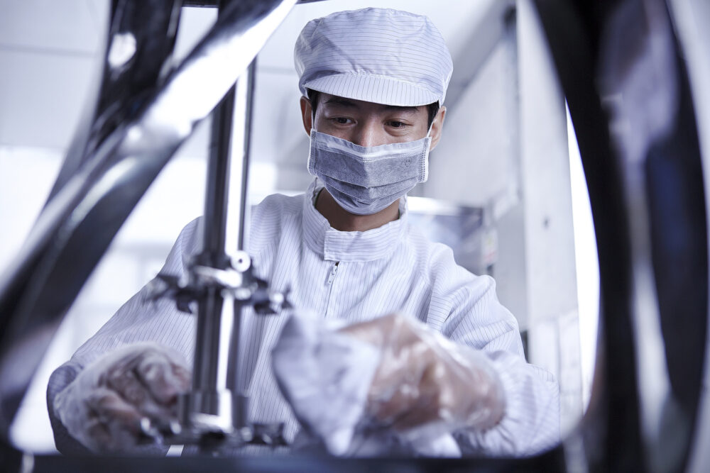 Clean room factory floor worker cleaning a machine in a science and technology image produced for a battery factory.