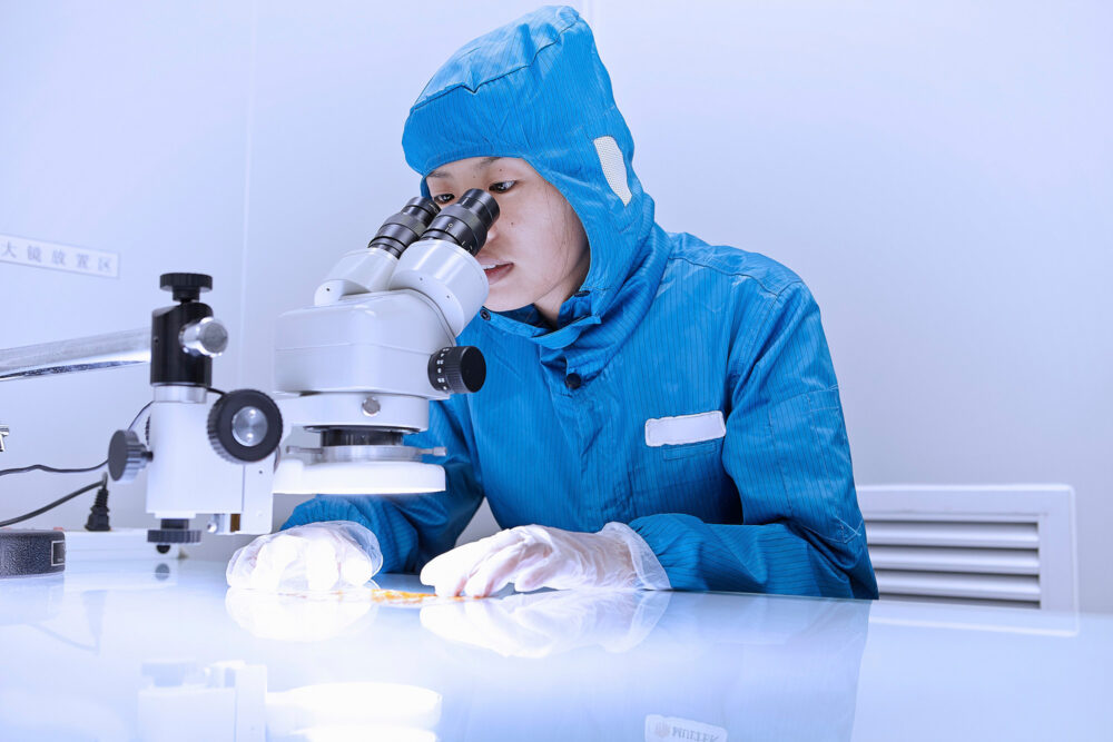 Young female engineer examining through a microscope in a clean room for Flextronics' science photography campaign.