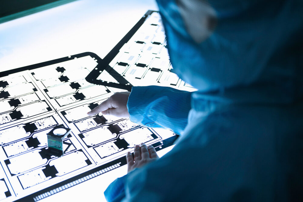 Scientist pointing to a blue plan in a clean room for Flextronics advertising and science photography content.